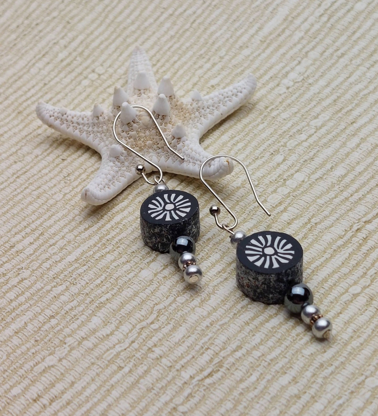 Polymer clay sunburst disk and hematite gemstone drop earrings with sterling silver ear wires leaning on starfish on linen background
