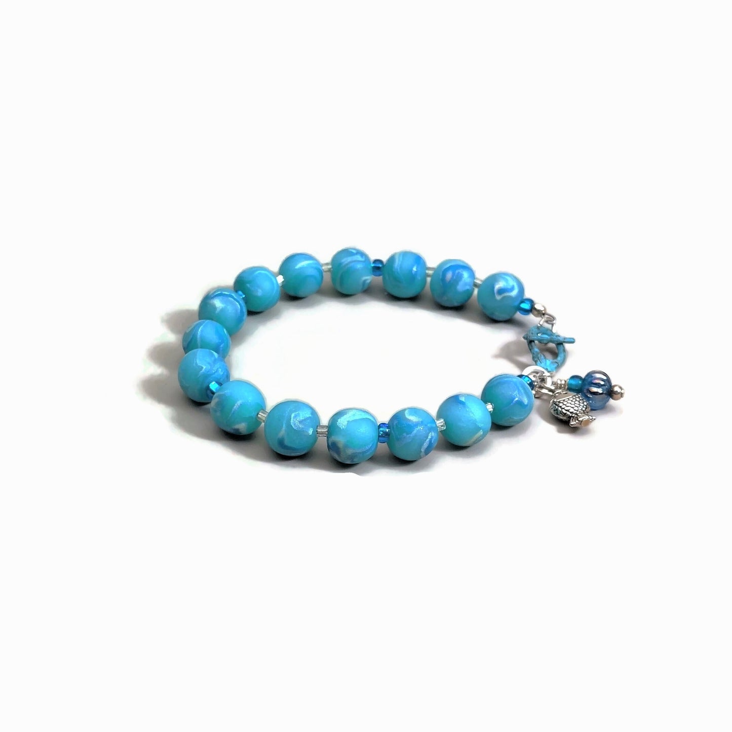 Round polymer clay bead bracelet with copper-plated patina toggle clasp, fish and bead charm on white background