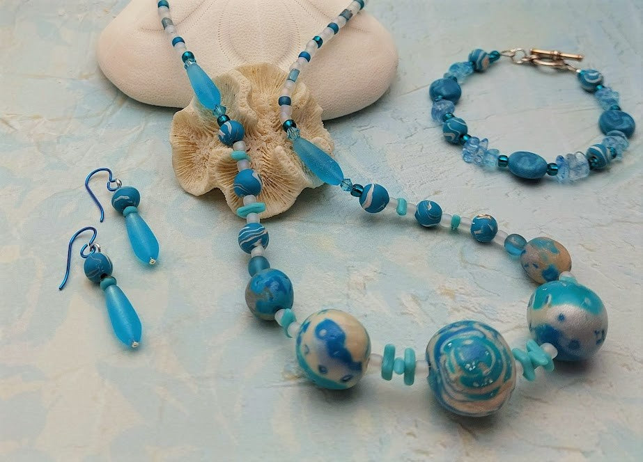 Polymer clay and glass bead necklace, drop earrings, bracelet with toggle clasp on light blue background