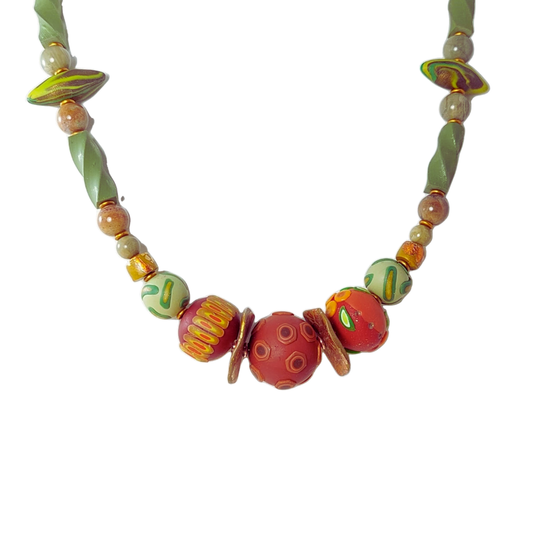 A handmade beaded necklace featuring a central cluster of red and orange patterned beads, flanked by green and yellow patterned beads and twisted green spacers, set against a plain white background.