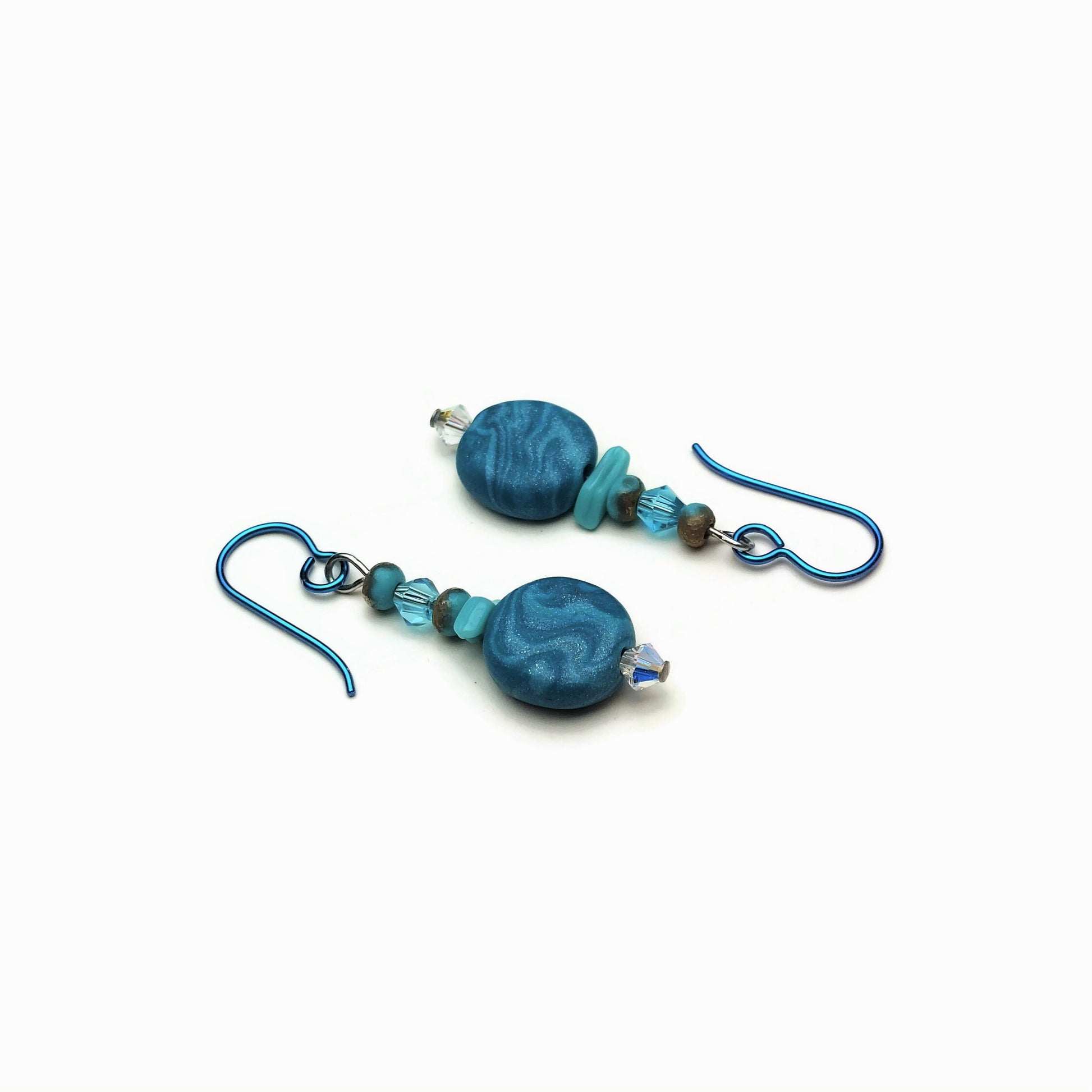 Polymer clay disk bead and crystal drop earrings with teal niobium ear wires on white background